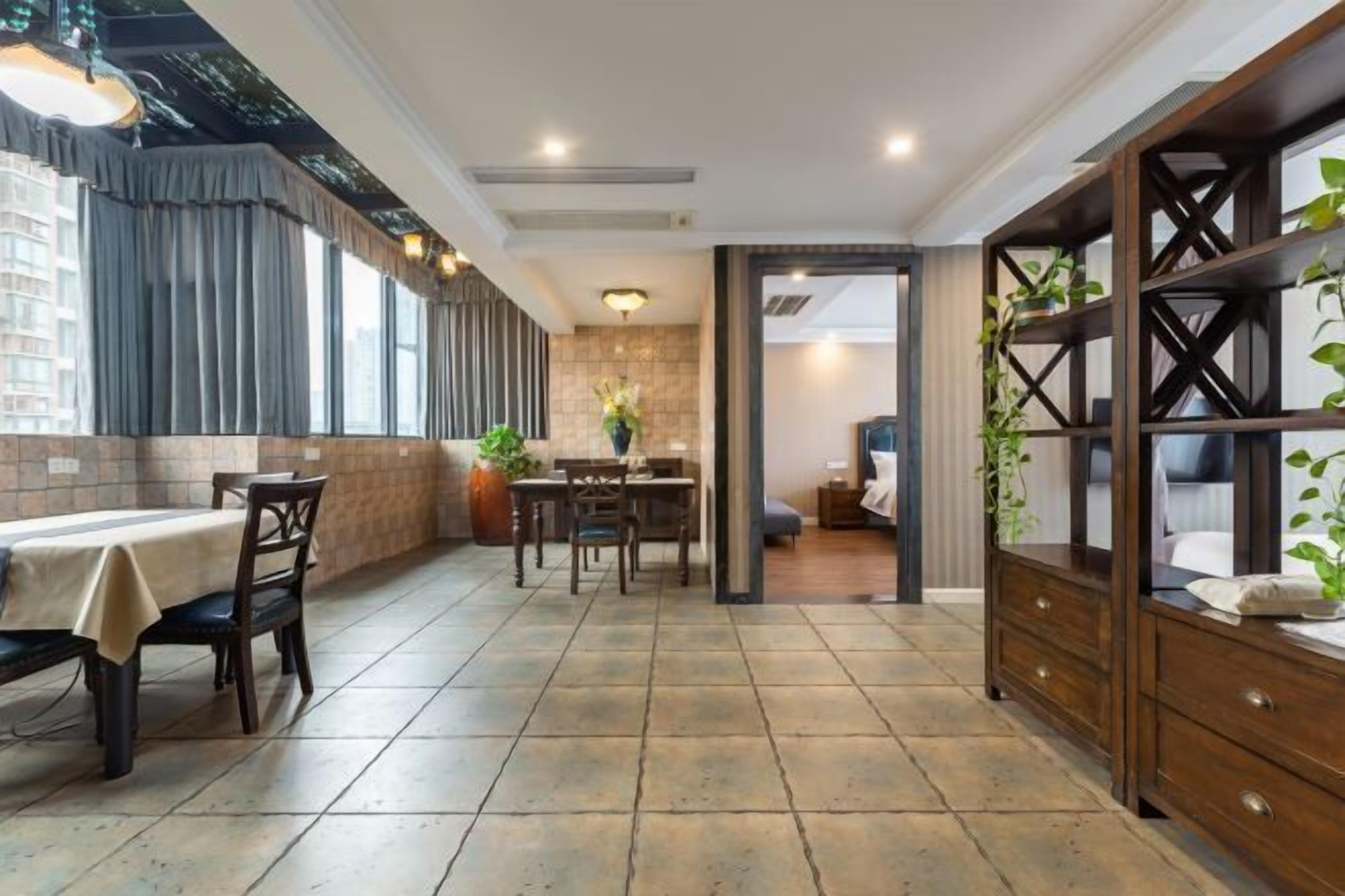 A dining area with a table and chairs, a wooden cabinet with shelves, and a view of the city through large windows.