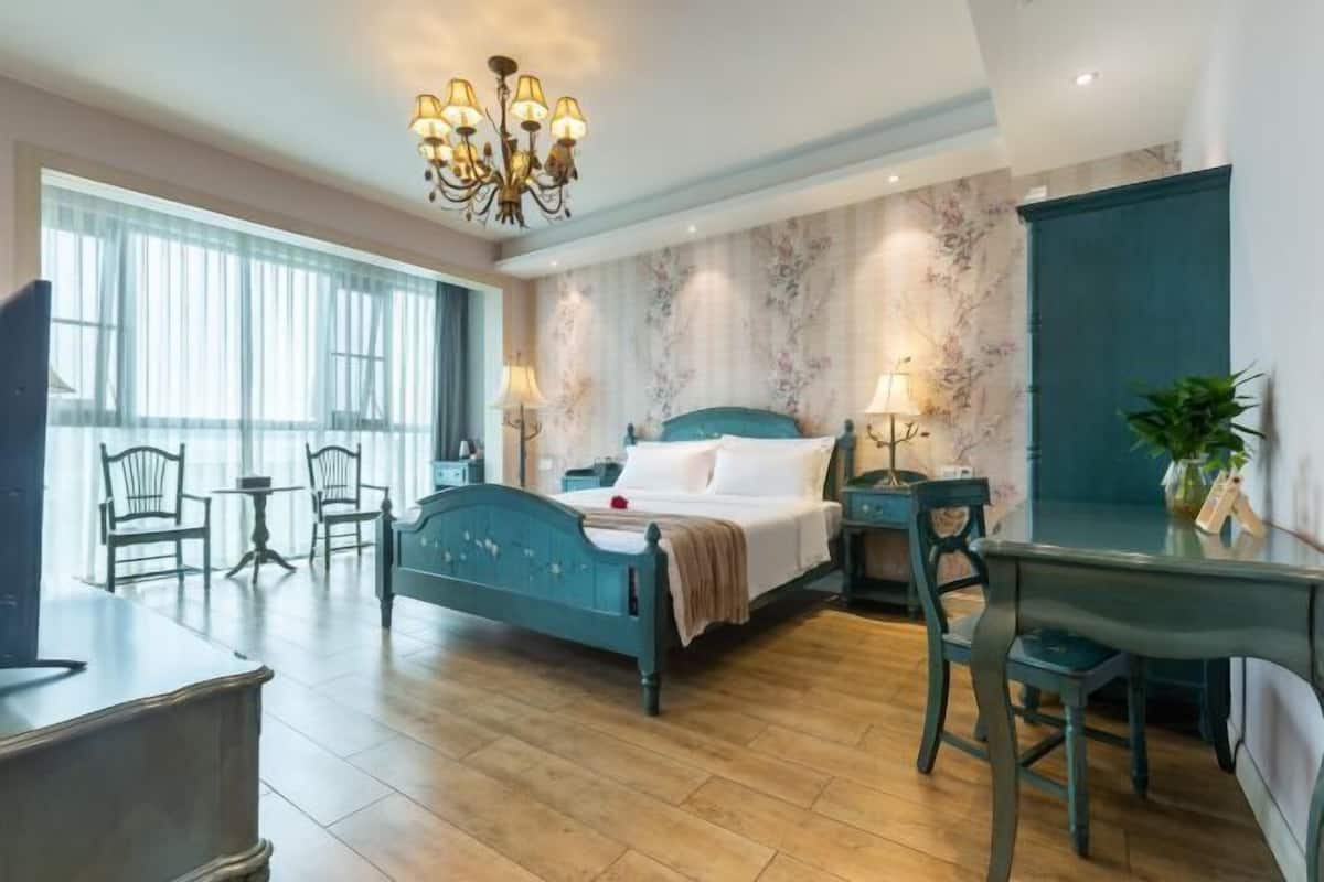 Quarto com cama, escrivaninha, cadeira, televisão e janela com cortinas.