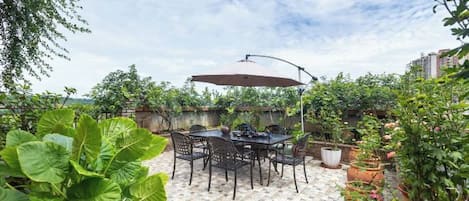 An outdoor patio with a table and chairs, surrounded by potted plants and a clear sky.