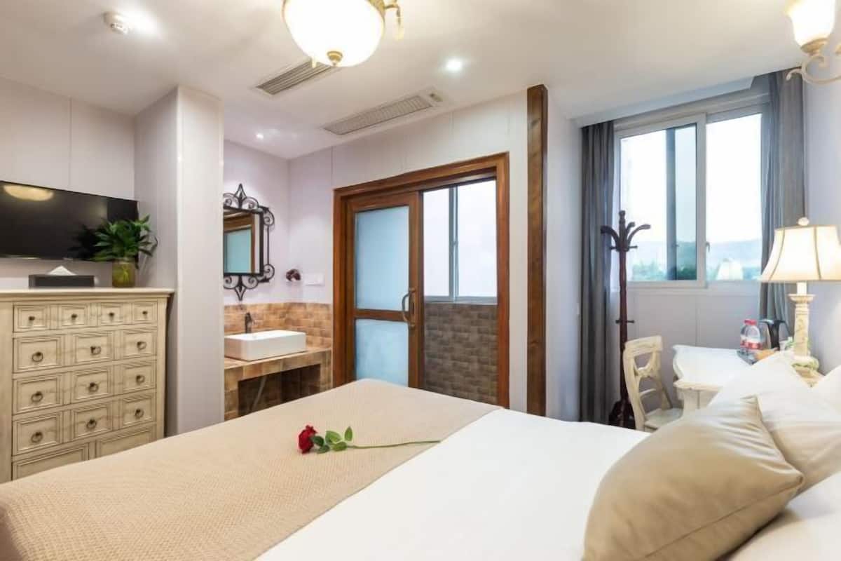 Quarto de hotel com cama, cômoda, televisão e janela com cortinas, oferecendo vista para o exterior.
