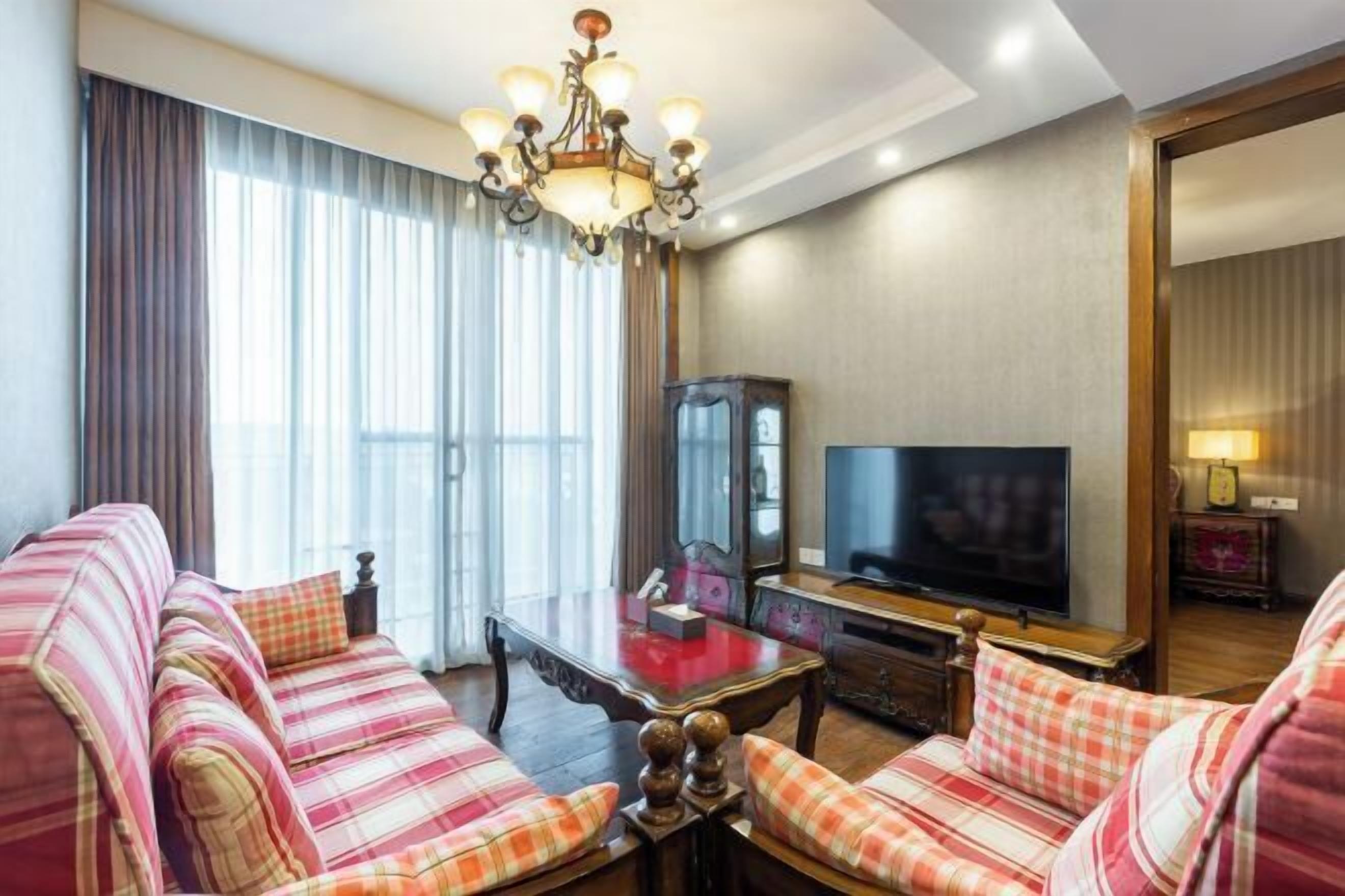 A hotel room with a sofa set, a television, a mirror, and a chandelier.
