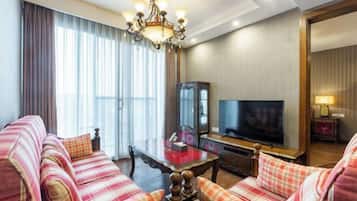 A hotel room with a sofa set, a television, a mirror, and a chandelier.