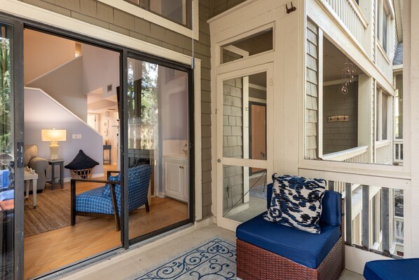 A modern interior with a glass door leading to a living area, a staircase, and a balcony with wicker furniture.