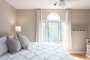 Een slaapkamer met een groot bed, een plafondventilator, een raam met gordijnen en een wandplank.