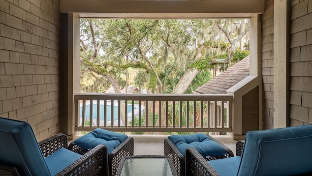A covered balcony with wicker furniture and a view of trees and a swimming pool.