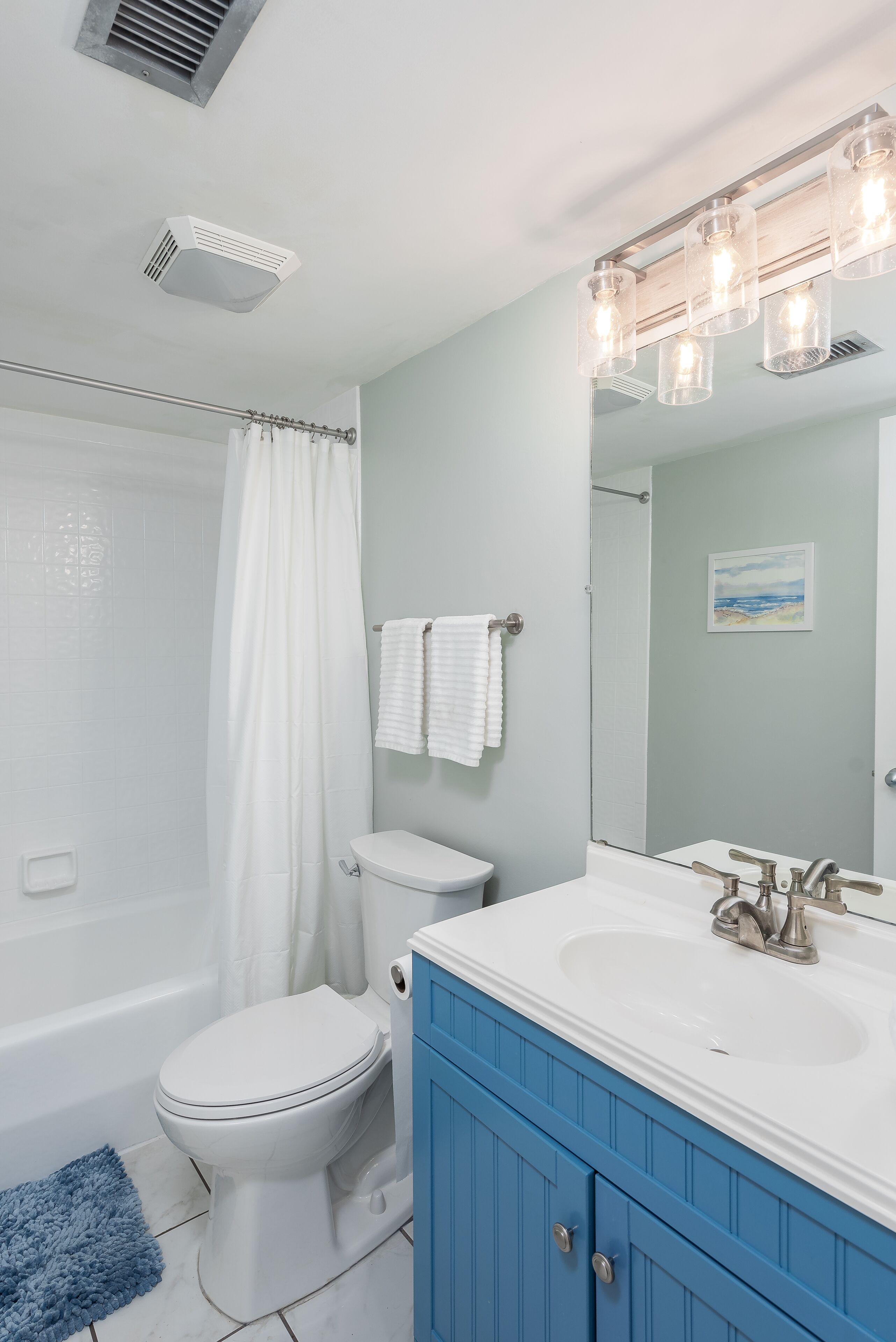 A bathroom with a white toilet, a blue vanity, a white sink, and a shower curtain.