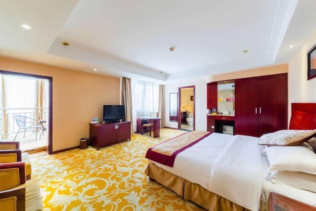 Habitación de hotel con cama, televisor, escritorio, silla, armario y balcón.
