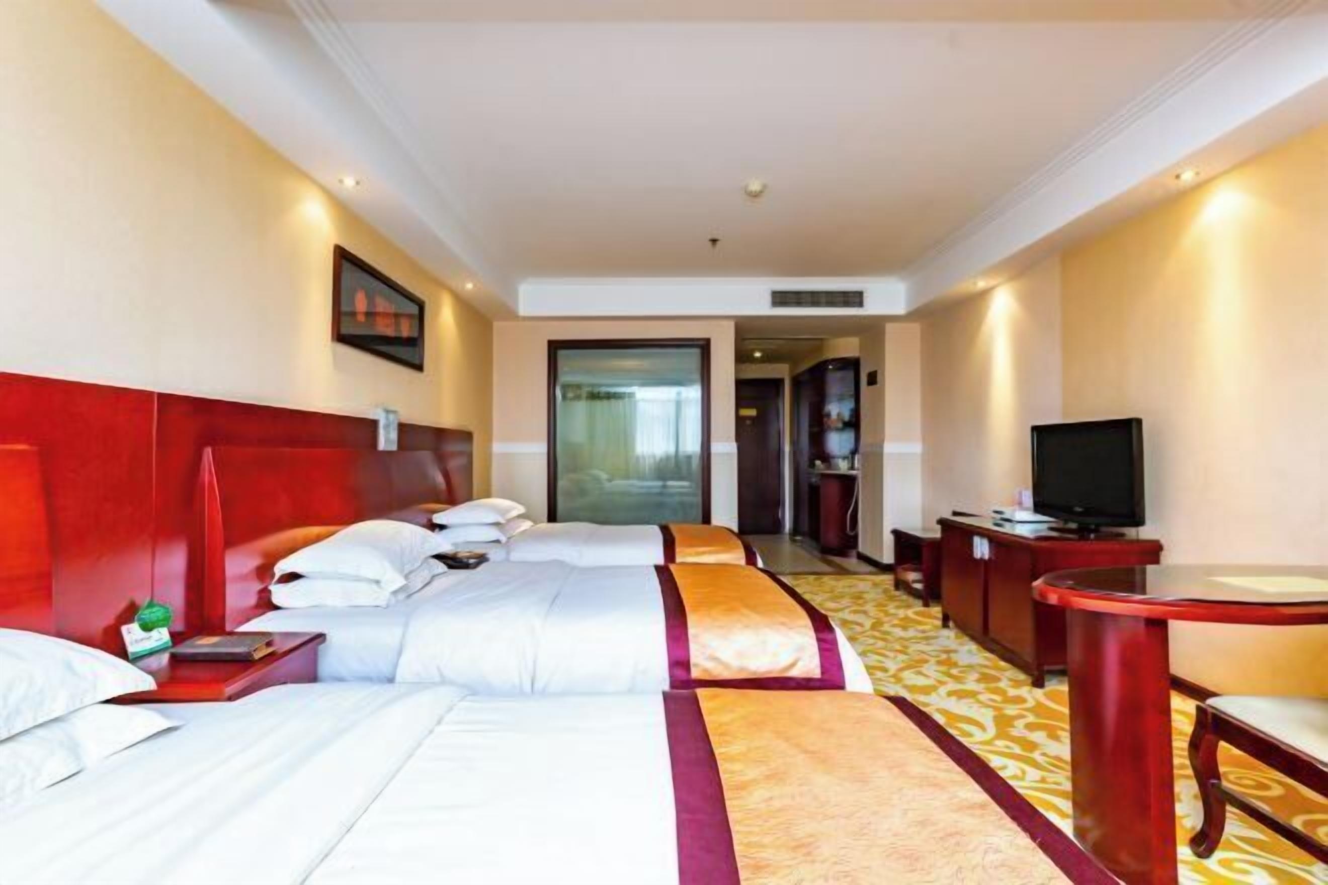 A hotel room with a bed, bedside table, TV, and a desk with a chair.
