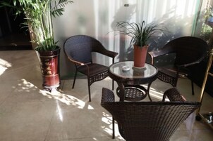 Un patio con paredes de vidrio, muebles de mimbre, plantas en macetas y una mesa de vidrio.