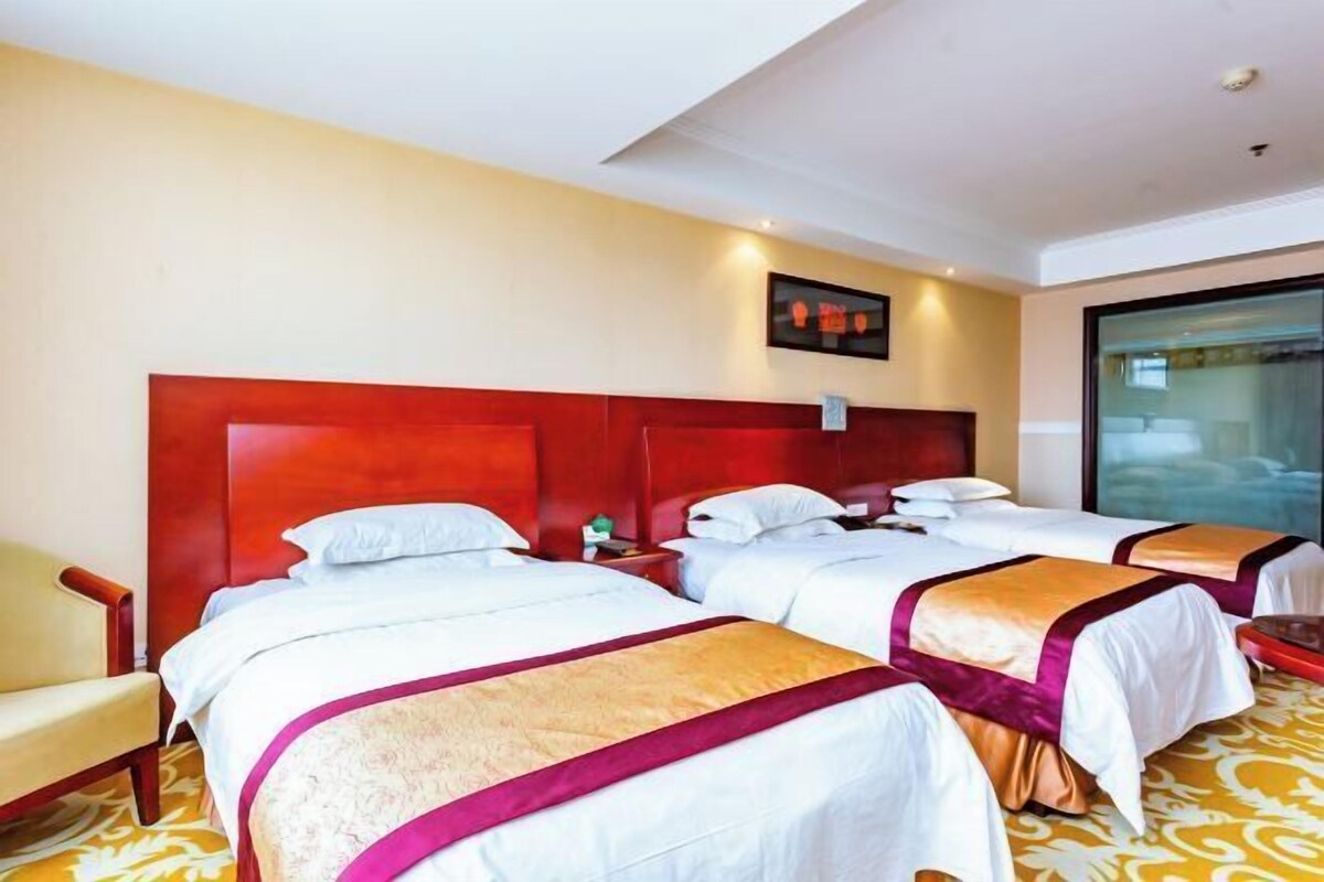Een hotelkamer met twee bedden, een houten hoofdeinde, een kleine tafel en een stoel.