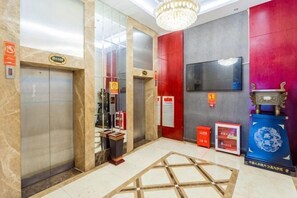 Zona de ascensores con puertas de vidrio, una pared roja, un televisor montado y un expositor azul.