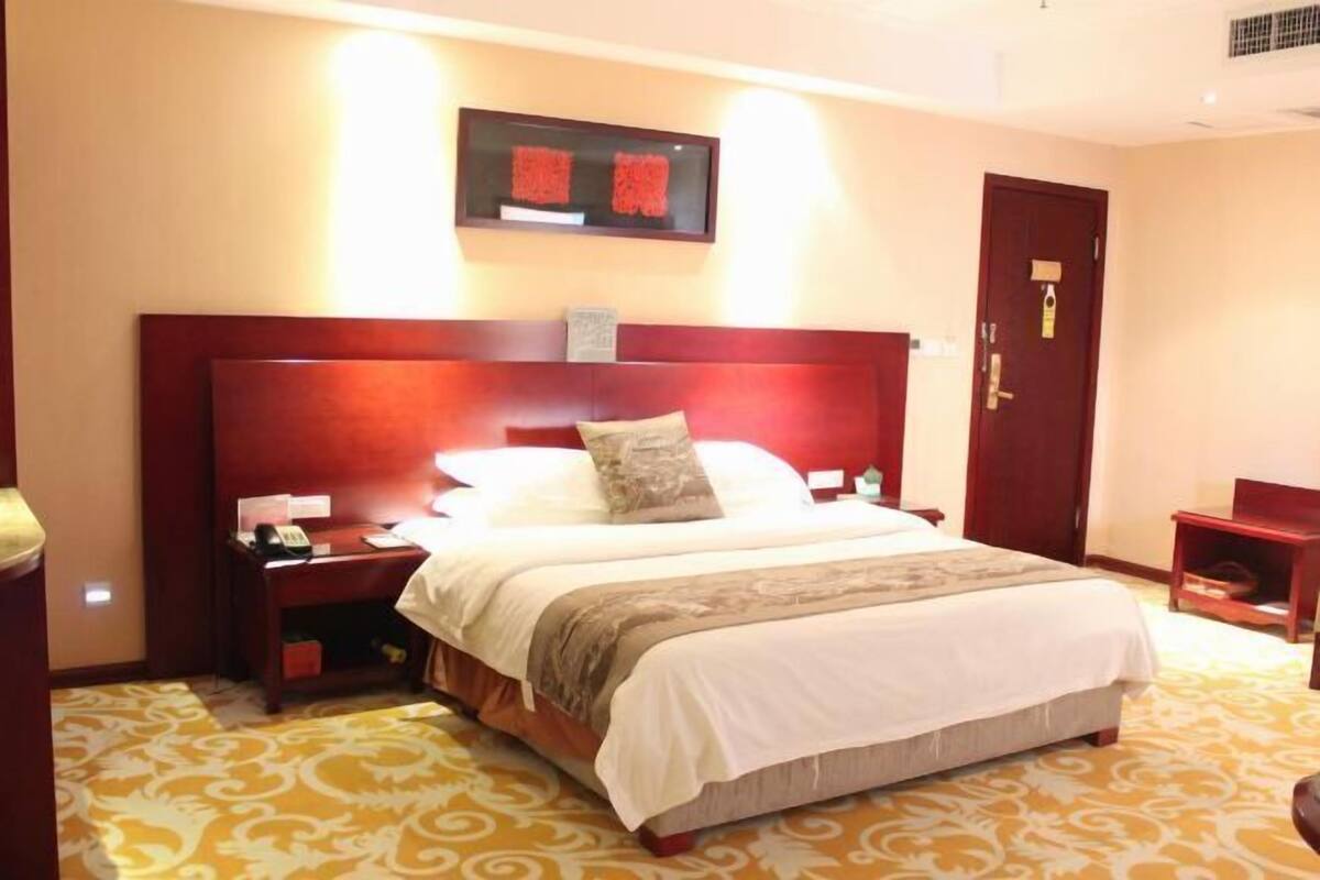 Una habitación de hotel con una cama grande, una mesita de noche, una obra de arte colgada en la pared y una puerta.