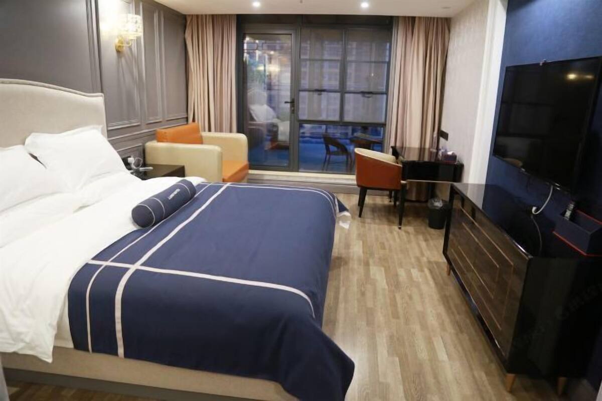 A hotel room with a large bed, a desk, a chair, a television, and a sliding glass door to the outside.