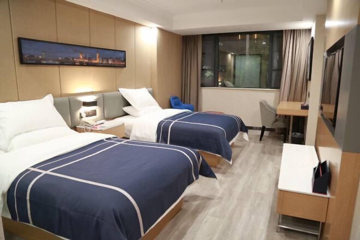 A hotel room with two beds, a desk, a chair, a TV, and a window with curtains.