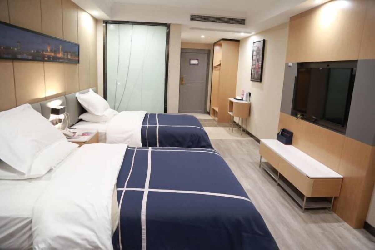 A hotel room with two beds, a desk, a TV, and a view of the cityscape.