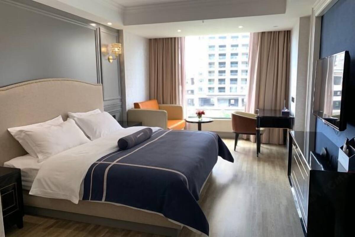 A hotel room with a bed, a desk, a chair, a TV, and a window with a city view.