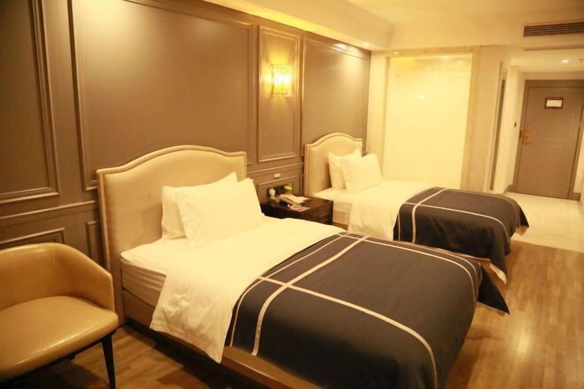 A hotel room with two beds, a nightstand, a chair, and a door.