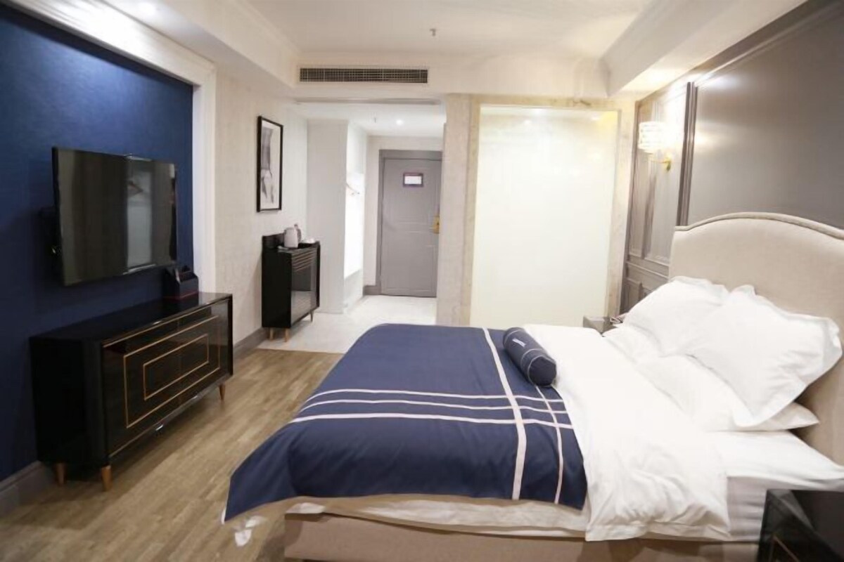 A hotel room with a bed, a TV on the wall, a dresser, and a door leading to another room.