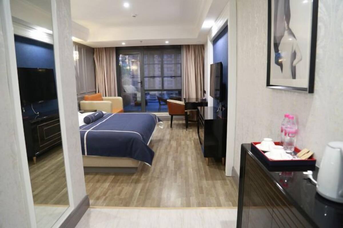 A hotel room with a bed, a desk, a TV, and a window with curtains.