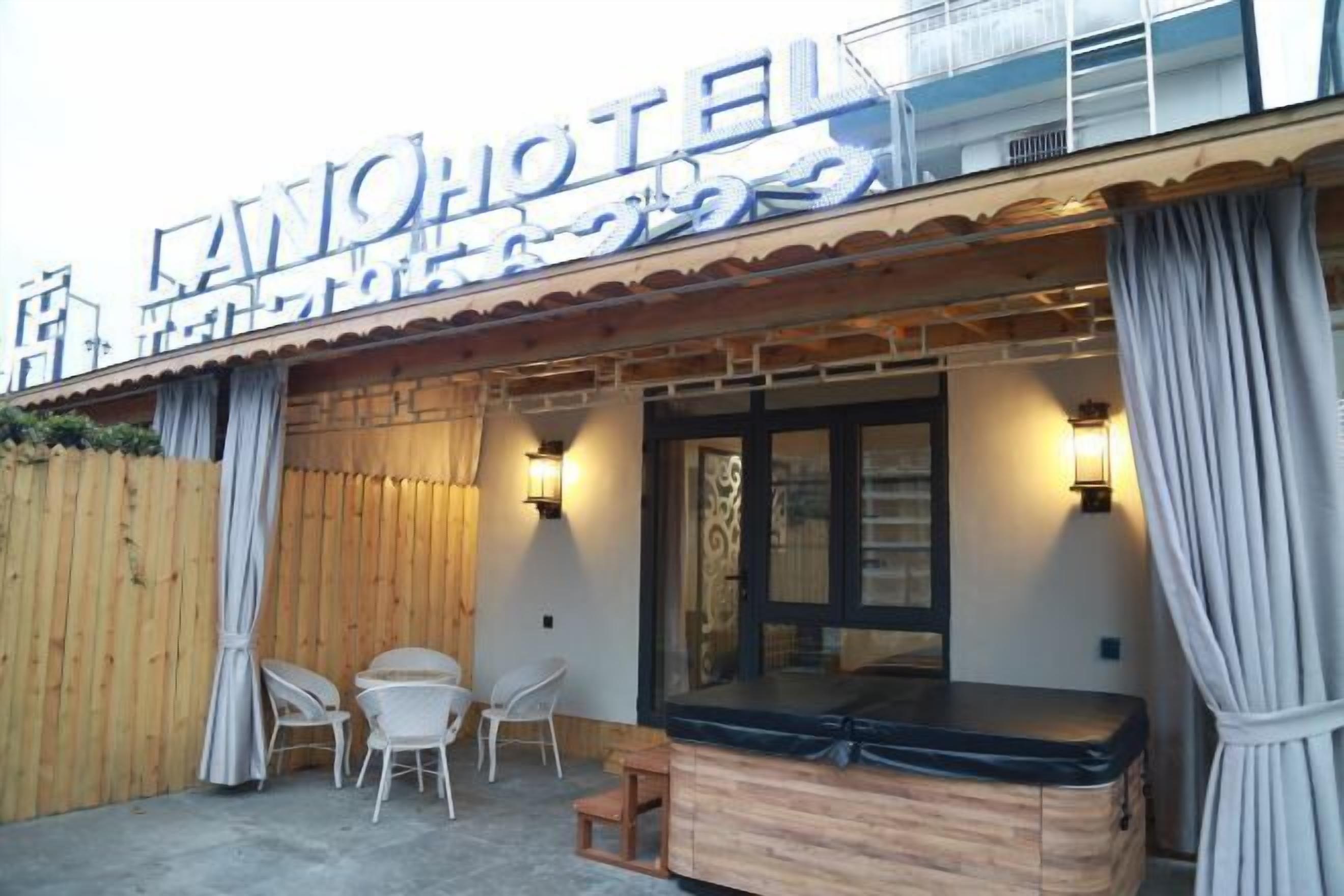 Exterior de un hotel con fachada de madera, zona de estar al aire libre cubierta con sillas y un jacuzzi.