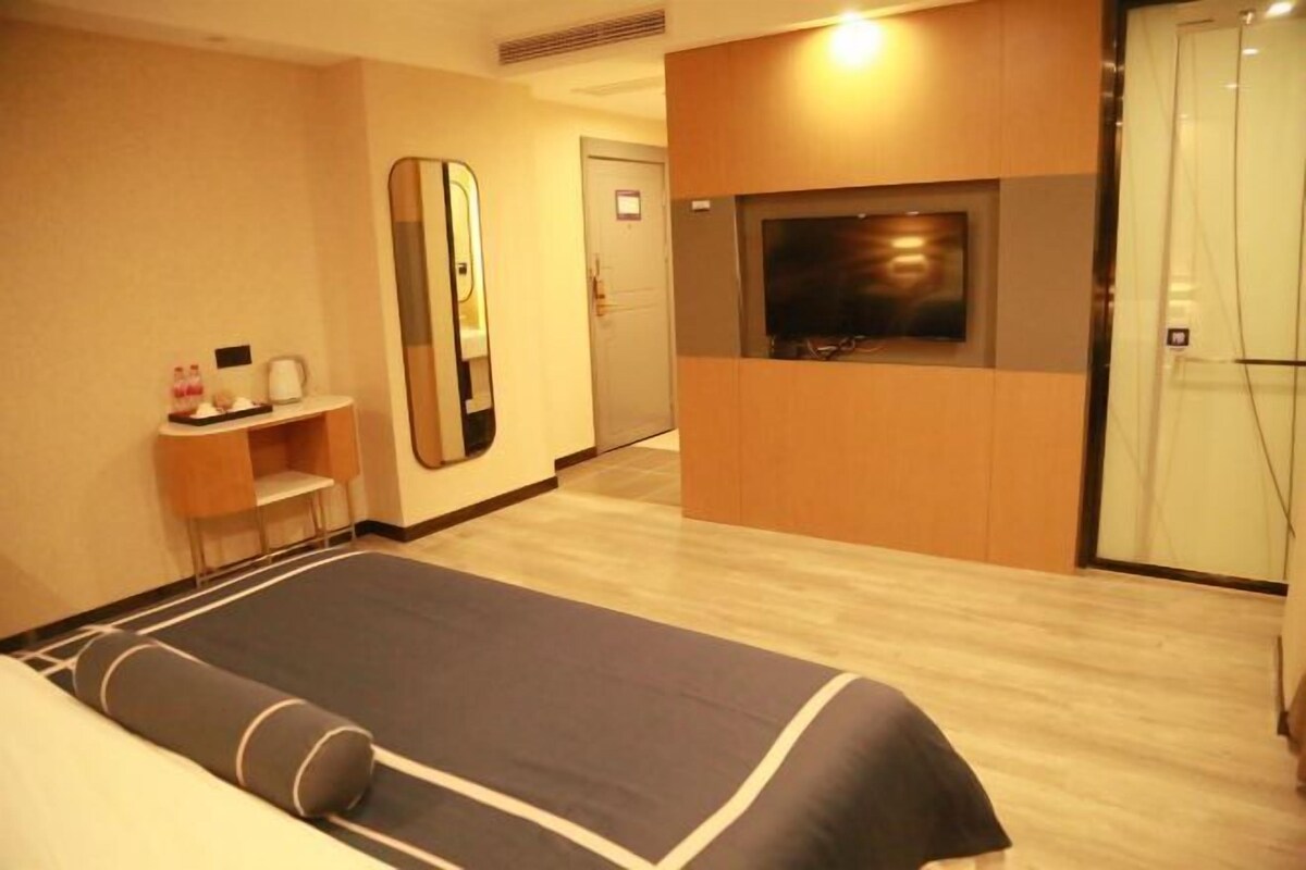 A hotel room with a bed, a mirror, a TV, and a small table with toiletries.