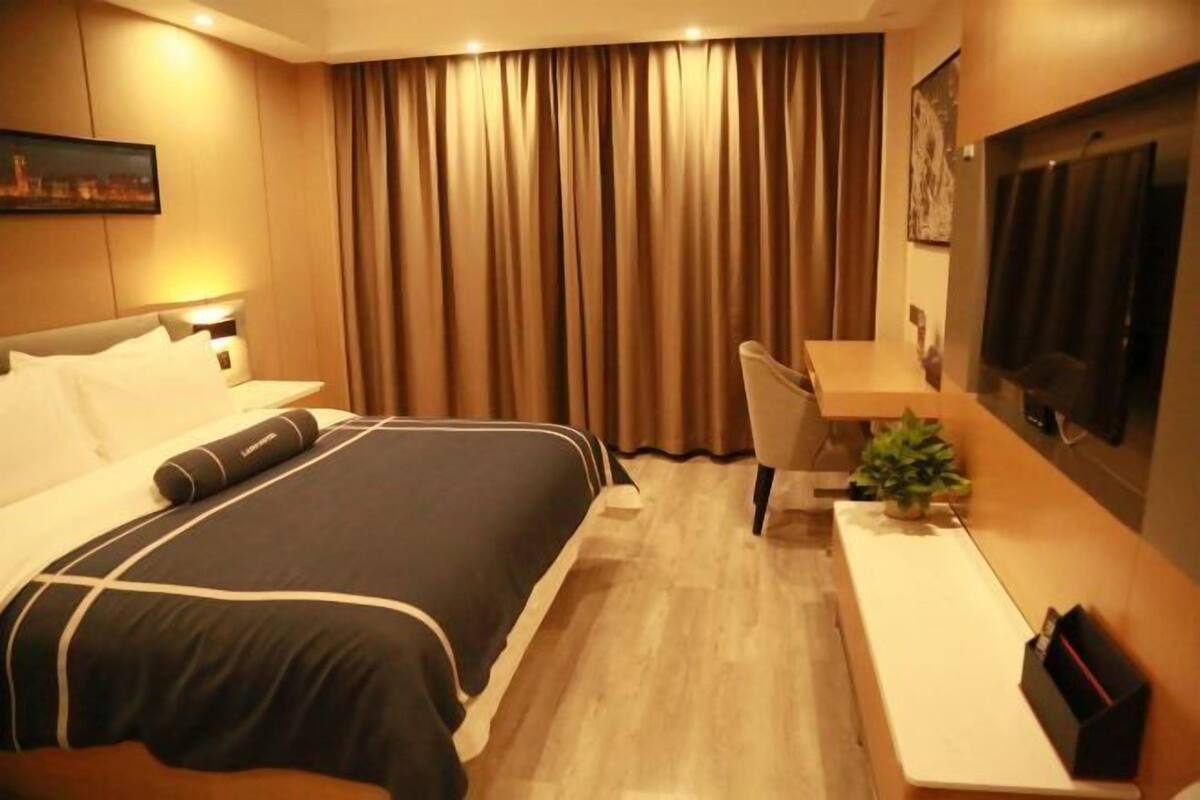 A hotel room with a bed, a desk, a chair, a TV, and a curtain.
