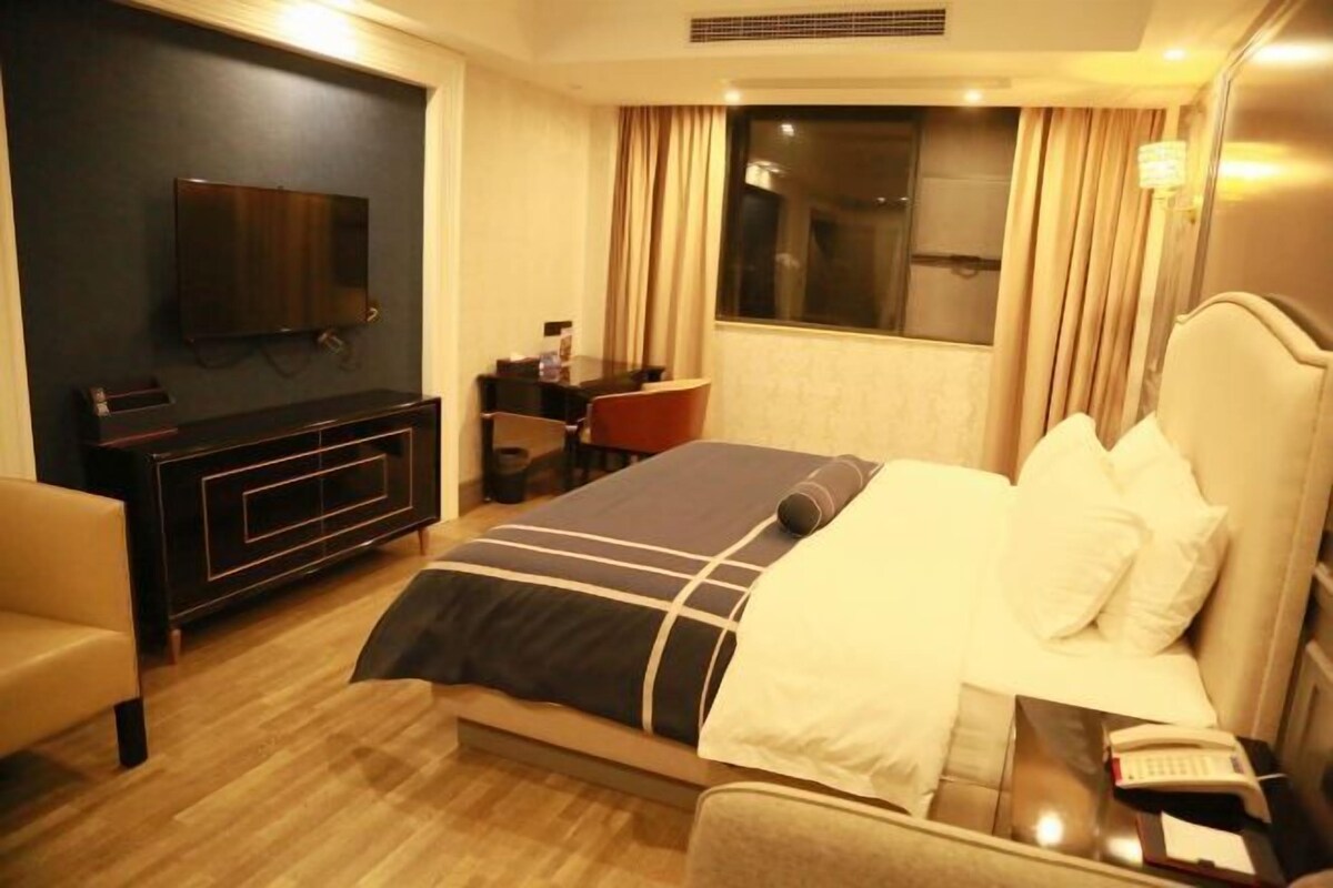 A hotel room with a bed, a desk, a chair, a TV, and a window with curtains.