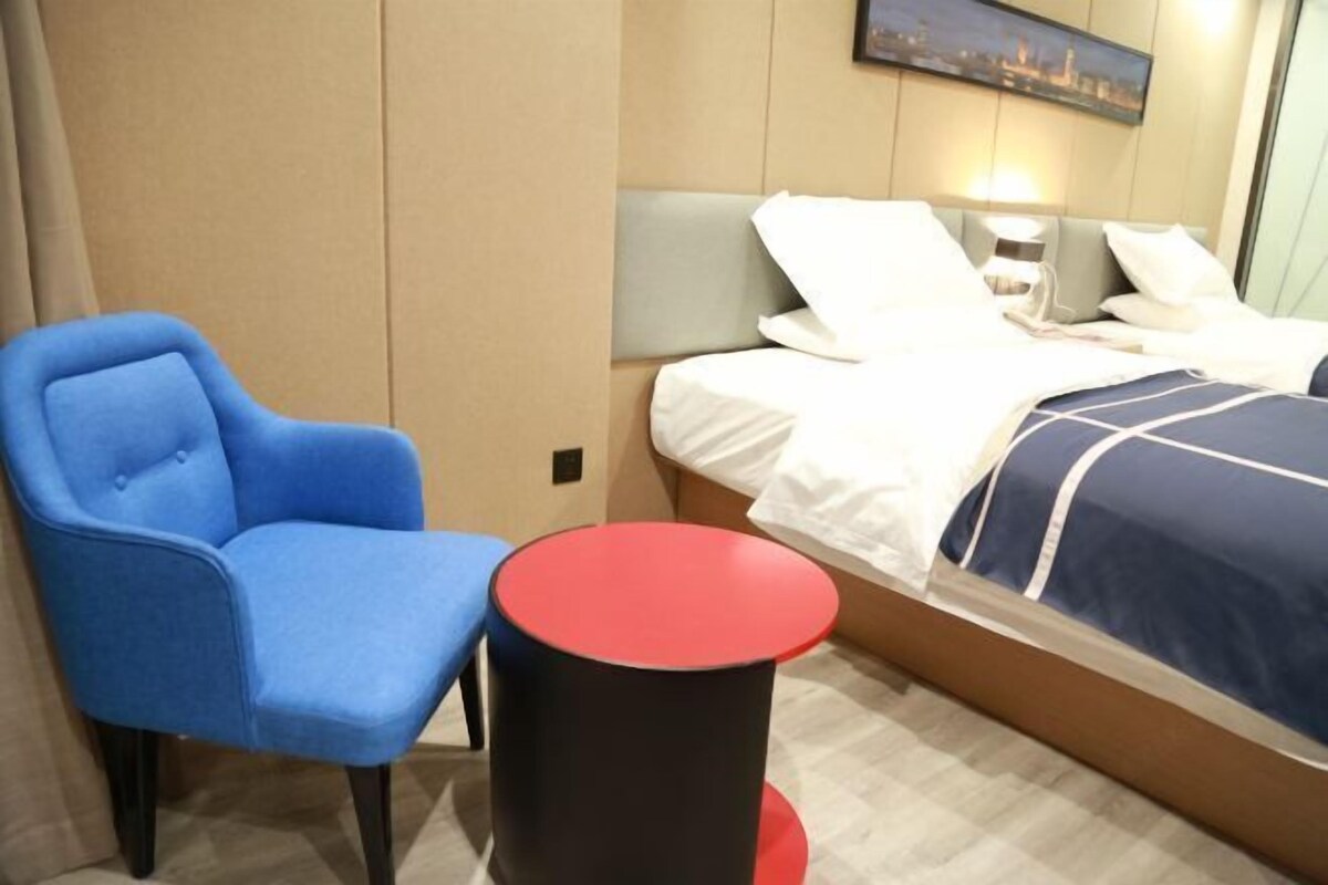 A hotel room with a bed, a blue armchair, and a small red table.