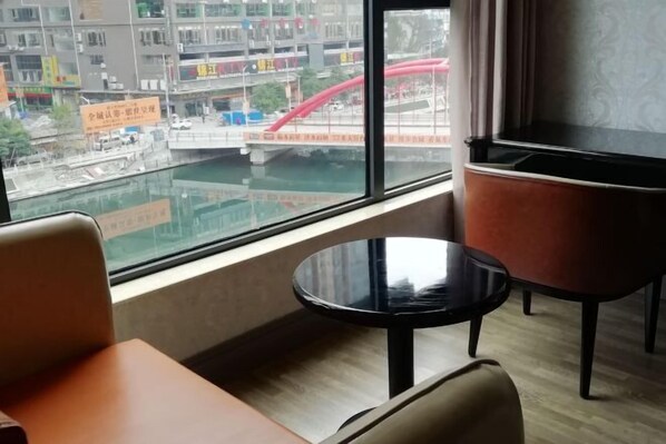 A hotel room with a large window offering a view of a cityscape, including a bridge and buildings. There is a round black table and a brown chair in the foreground. - lanyi Hotel (Guiding)
