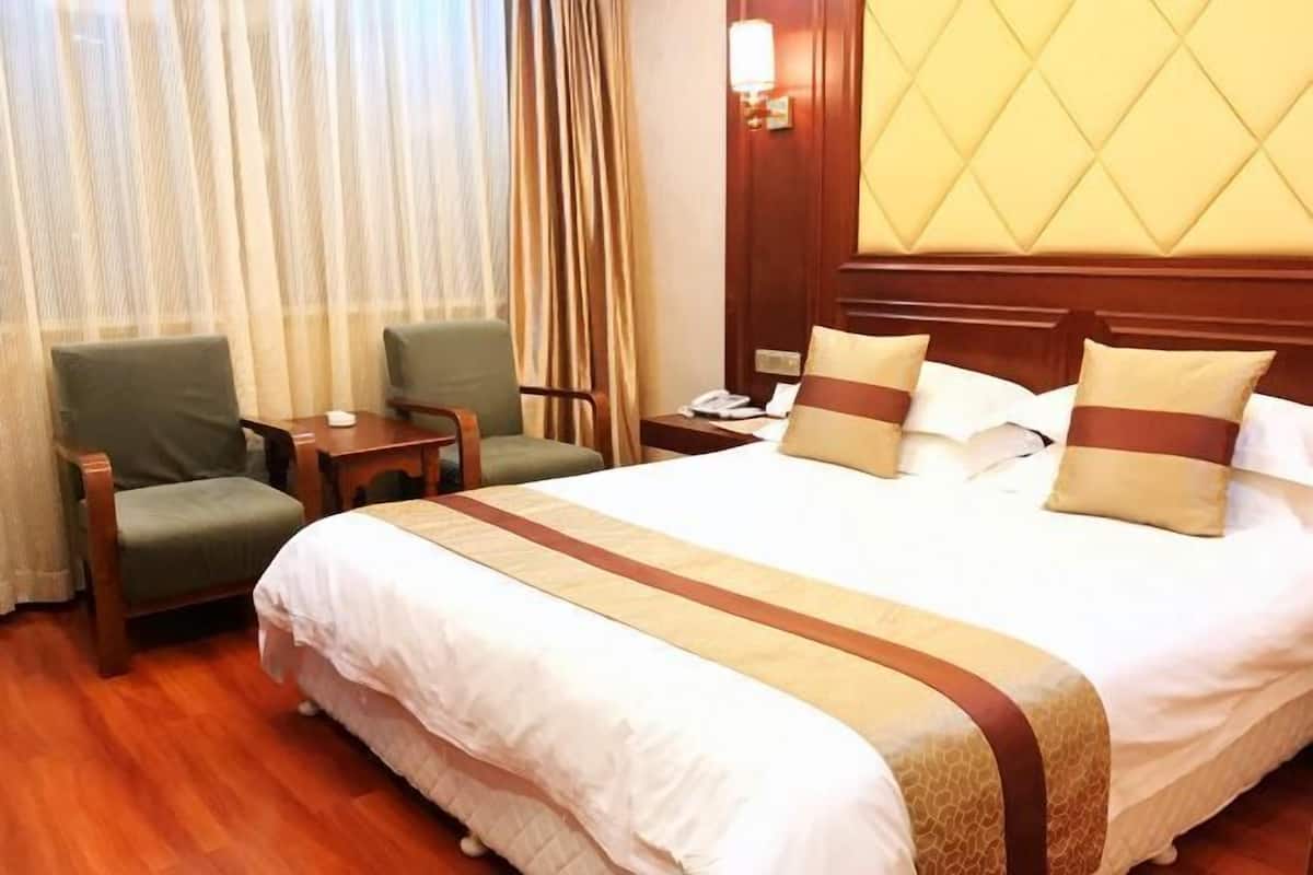 A hotel room with a large bed, two armchairs, a small table, and a nightstand with a lamp.