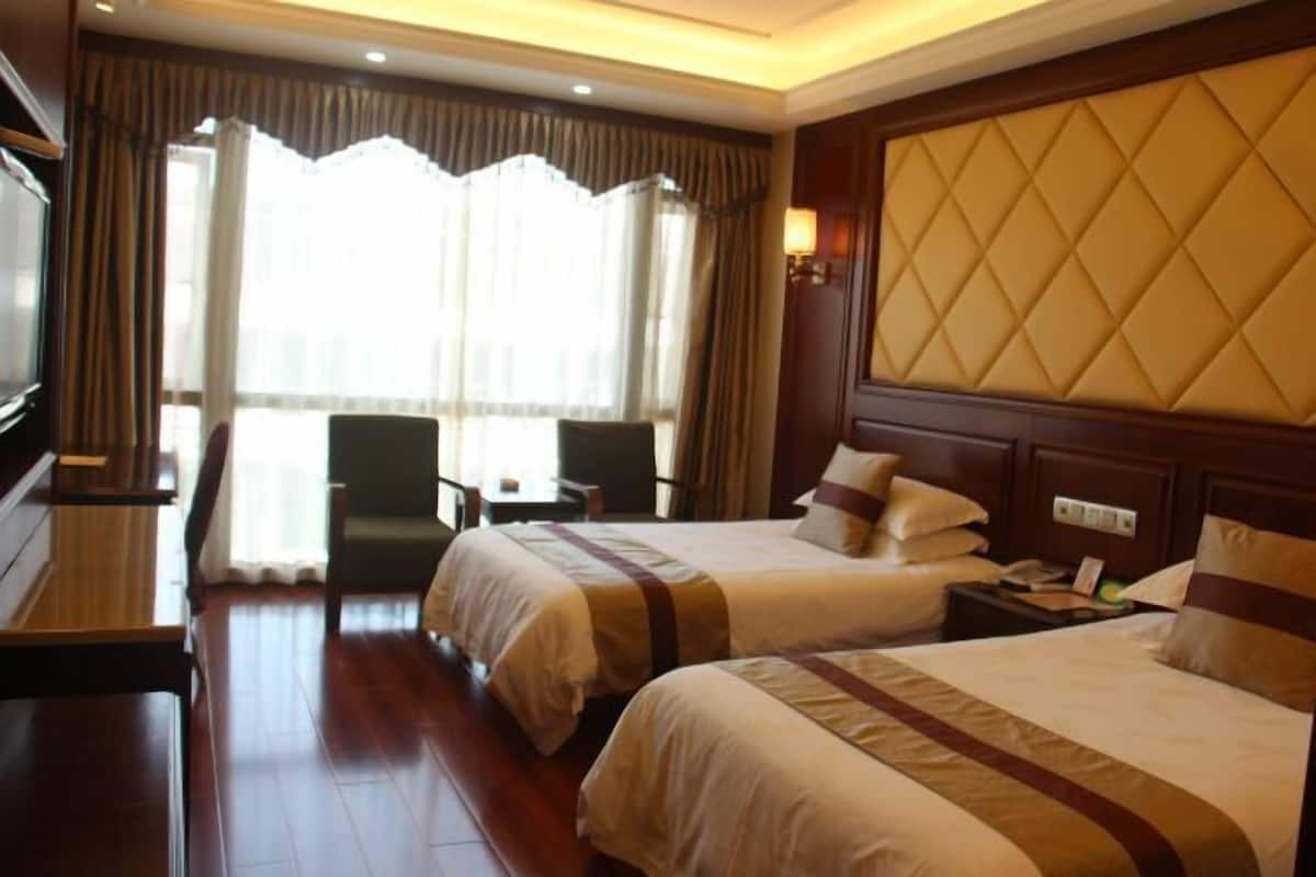 A hotel room with two beds, a desk, a chair, and a large window with curtains.