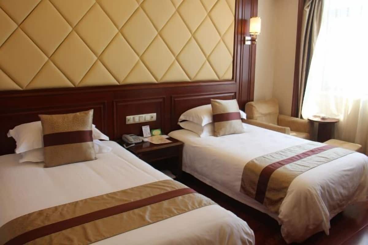 A hotel room with two beds, a wooden headboard, a nightstand with a phone, and a chair.