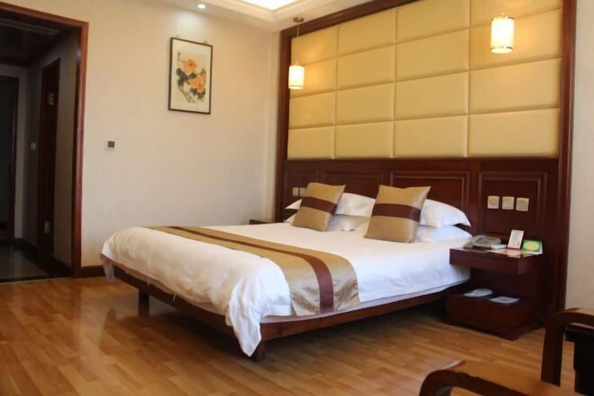 A hotel room with a large bed, wooden headboard, bedside tables, and a painting on the wall.