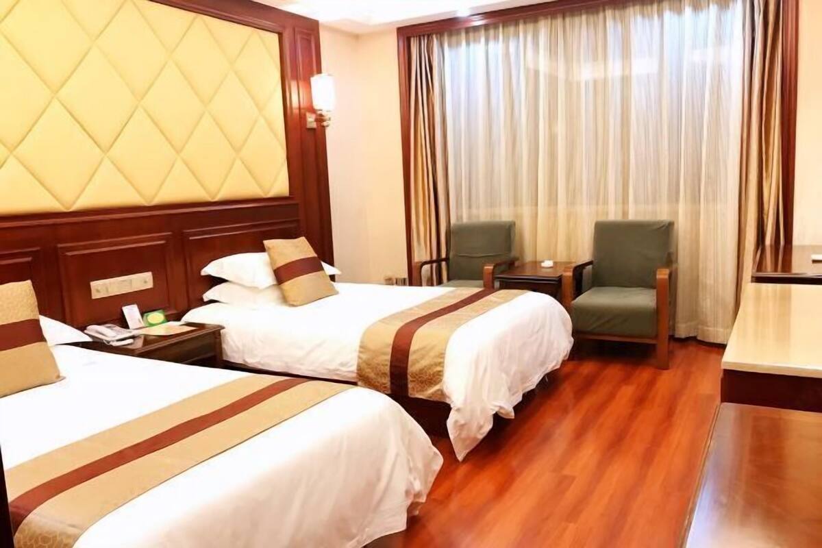 A hotel room with two beds, a desk, a chair, and a large window with curtains.