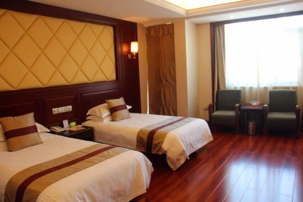 A hotel room with two beds, a wooden floor, a large window with curtains, and a small table with chairs.