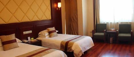 A hotel room with two beds, a wooden floor, a large window with curtains, and a small table with chairs.