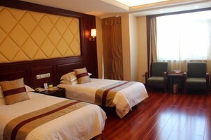 Quarto de hotel com duas camas, piso de madeira, uma janela grande com cortinas e uma pequena mesa com cadeiras.