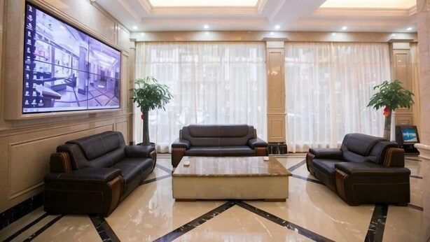 A spacious lobby with a large flat-screen TV, two leather sofas, a coffee table, and a marble floor. - Baiweilin Hotel (Cangnan)