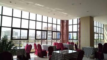 A spacious indoor area with tables and chairs arranged for dining, large windows offering a view, and a modern architectural design.