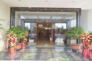 Entrada de hotel con puerta de vidrio, plantas en macetas y una pared azul a rayas.