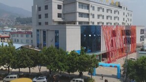 A multi-story building with a modern architectural design, featuring a prominent entrance with a blue canopy and red decorative elements. - Guyuecun Hotel (Yongde)