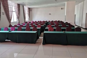 Una sala de conferencias con mesas y sillas en fila, ventanas amplias y una pizarra.