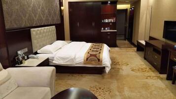 A hotel room with a large bed, a sofa, a TV, a wardrobe, and a desk with a lamp.