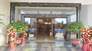 A hotel entrance with a glass door, potted plants, and a reception desk visible through the door. - Guyuecun Hotel (Yongde)