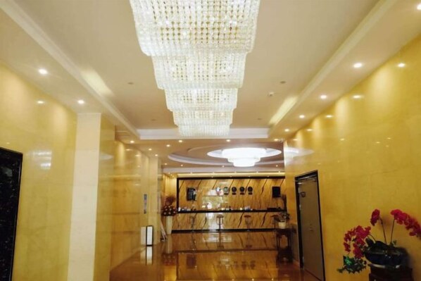 A hotel lobby with a large chandelier, a reception desk, and a polished floor.