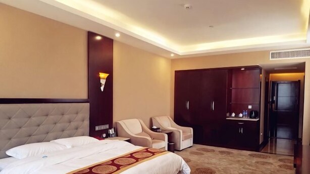A hotel room with a large bed, two armchairs, a wardrobe, and a desk. - Guyuecun Hotel (Yongde)