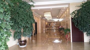 A hotel lobby with a polished marble floor, large potted plants, and a chandelier.