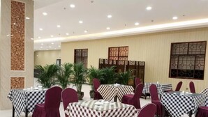 A dining area with checkered tablecloths, red chairs, and potted plants. - Guyuecun Hotel (Yongde)