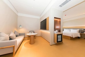 Una habitación de hotel moderna con sofá, mesa de comedor, televisor, cama y un pequeño armario.