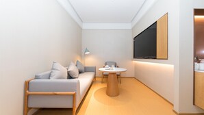 Ein modernes, helles Zimmer mit einer Couch, einem runden Tisch und einem an der Wand montierten Fernseher.